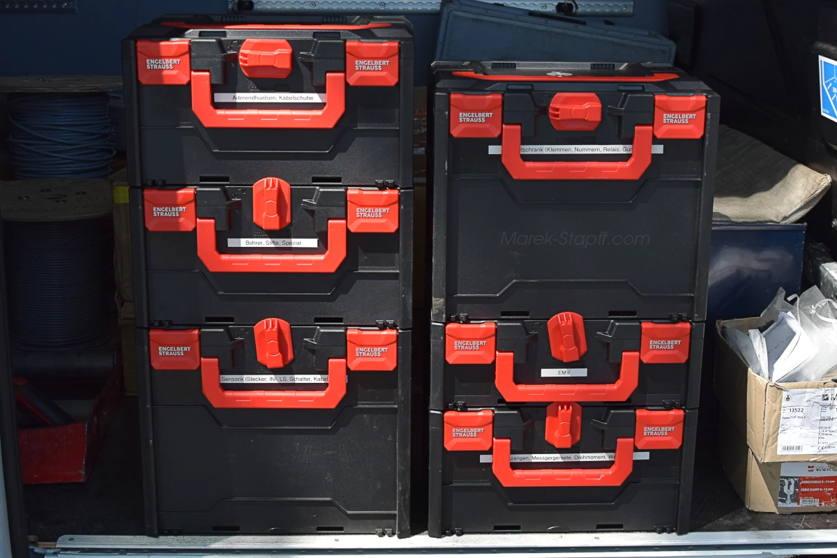 Beschriftete schwarz-rote Transportboxen, gestapelt und einsatzbereit im Laderaum eines Fahrzeugs – das geordnete Materiallager des Automatisierers